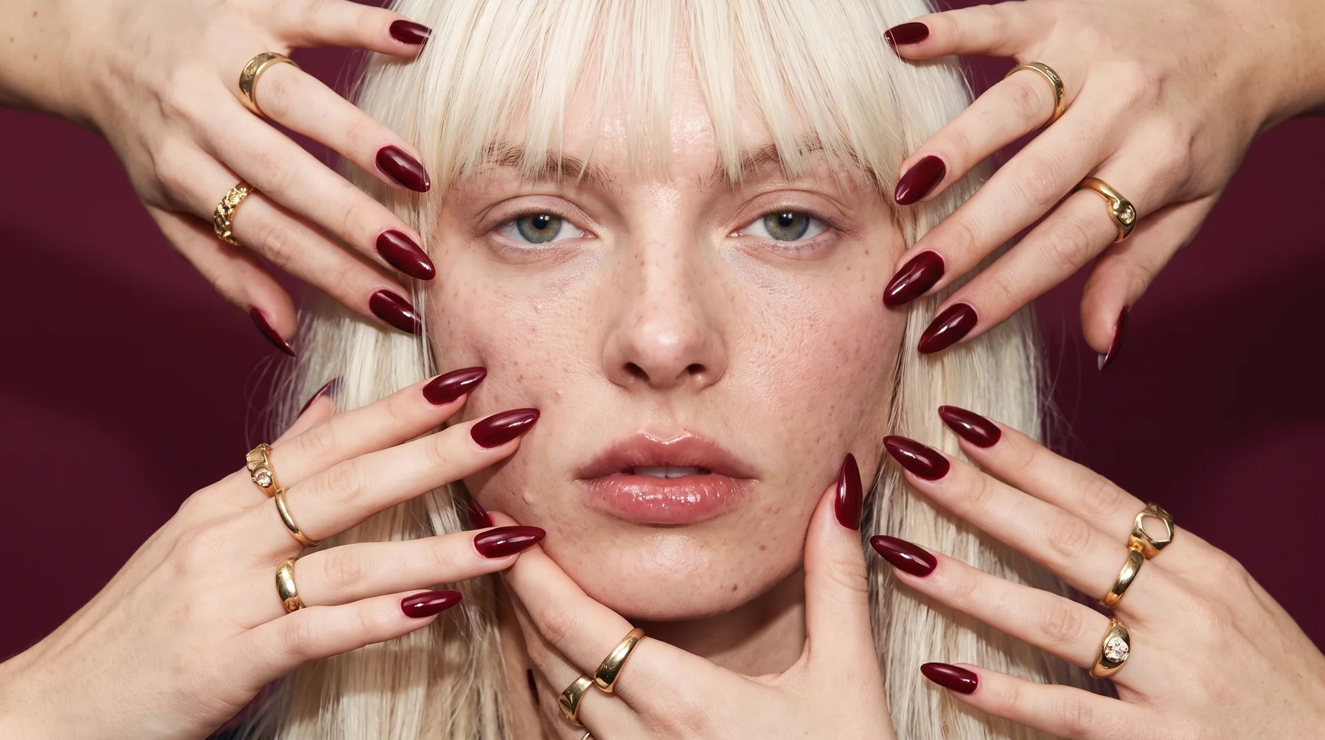 Quatre mains aux ongles grenat entourent son visage