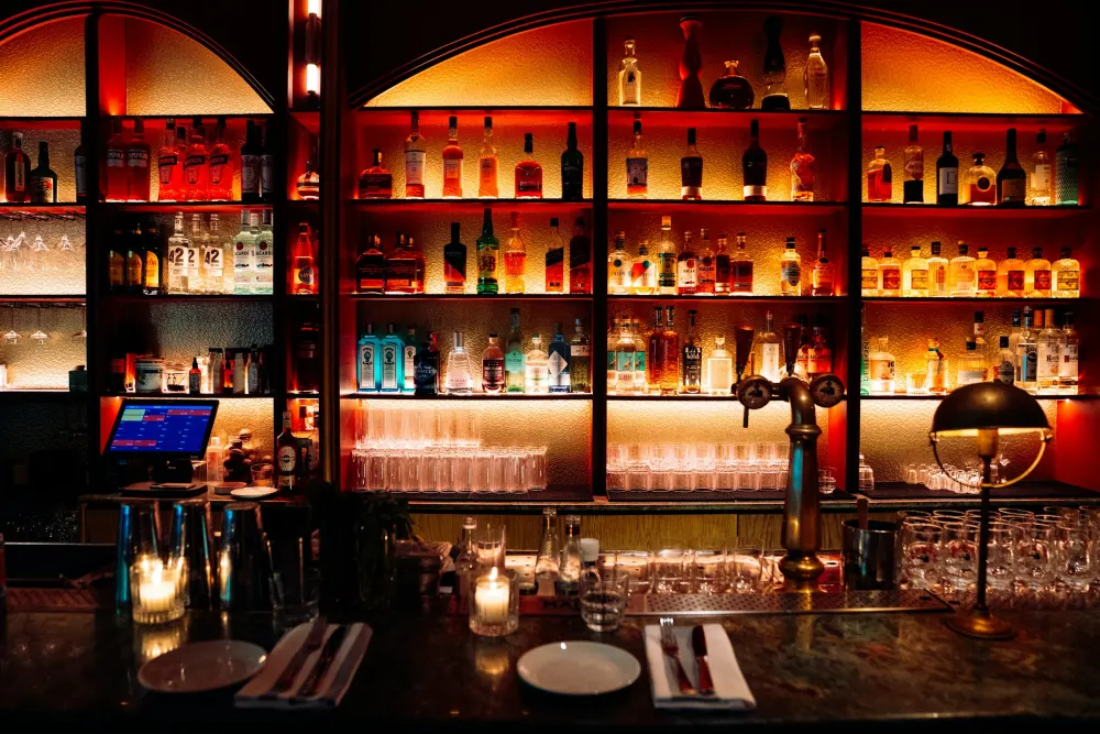 A back bar of glowing bottles under arches, candles on the counter