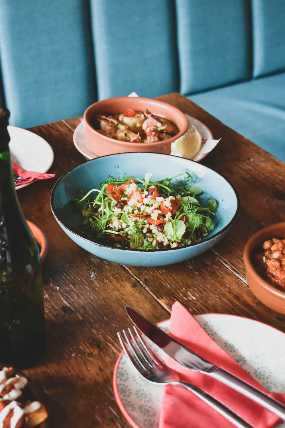Shared plates on a wooden table: a green salad, a small stew and dips